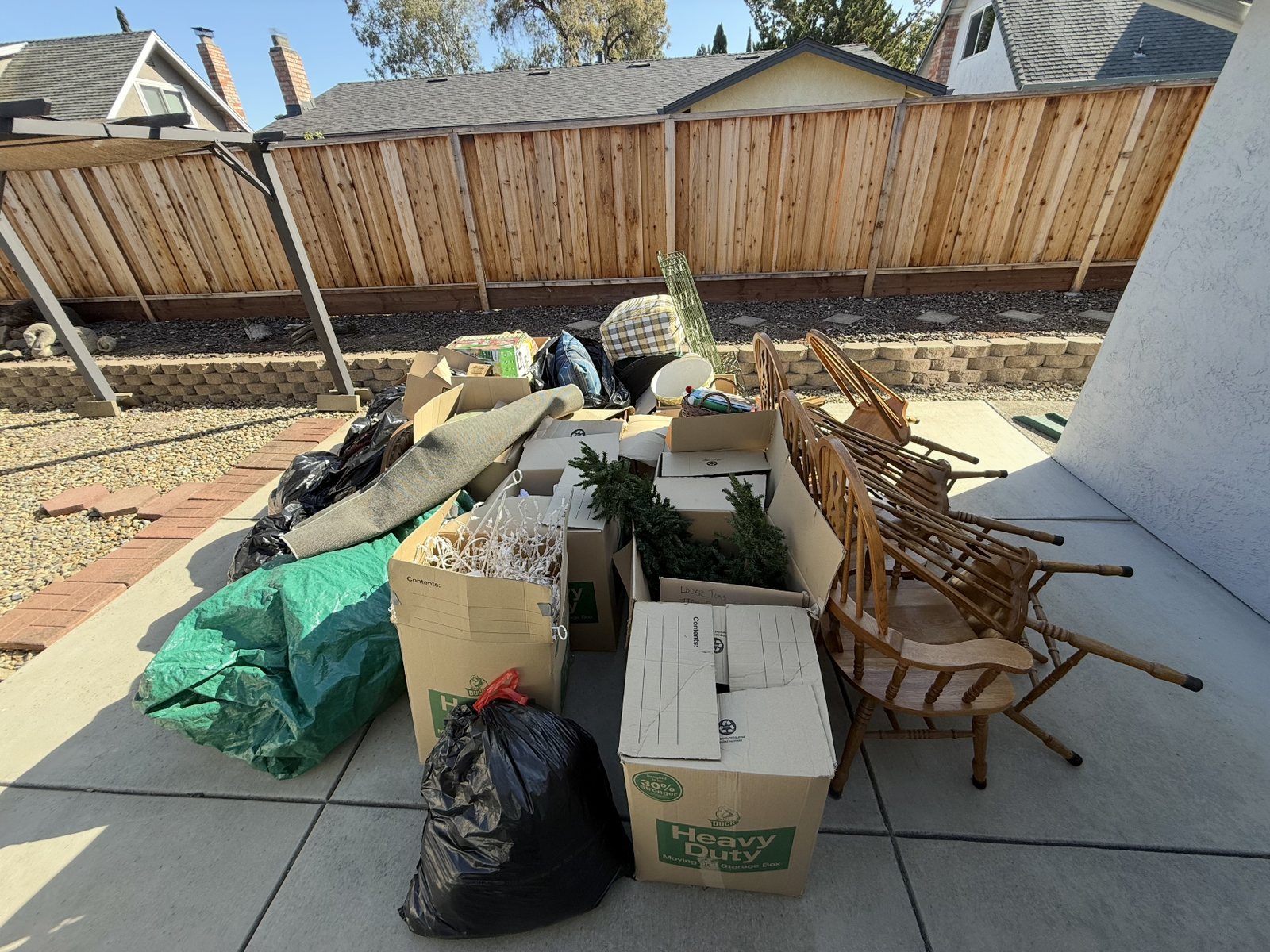 Back patio in Elk Grove, CA piled with boxes, bags, a rolled rug and old dining chairs before a junk removal cleanout